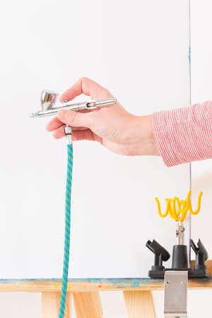 Hand holding a professional airbrush over white canvas or backgroundの写真素材