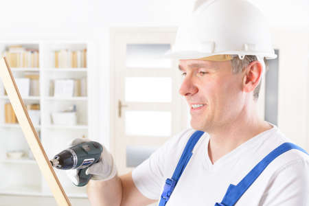 Smiling man with small wireless drill wearing protective helmet and glasses