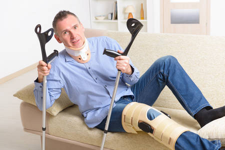 Man with leg in neck brace, knee cages and crutches for stabilization and getting up for...