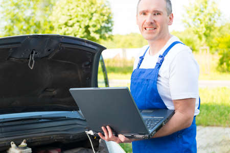 Mobile car service engineer checking car with his laptop on the road