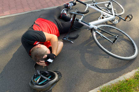 Bicycle accident. Biker lying on the road and holding his headの写真素材