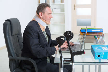 Businessman at work wearing neck brace with crutchesの写真素材