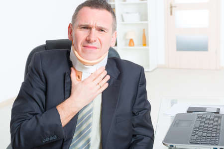 Businessman at work wearing neck braceの写真素材