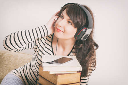 Woman listening an audiobook on smartphone sitting between piles of paper books on the floorの写真素材