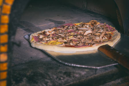Fresh original Italian pizza on a shovel is putting in a traditional wood-fired stone oven.の写真素材