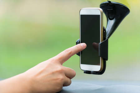 Hand touching screen on smart phone in the car holder to change naigation options or write SMS