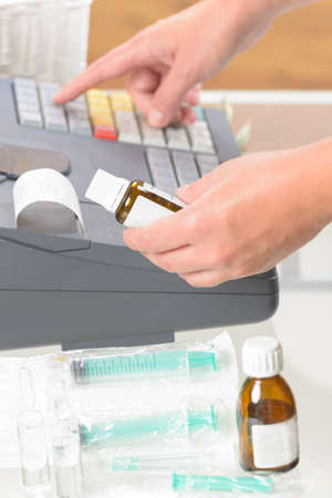 pharmacist holdnig bottle of medicine and using cash register at pharmacyの写真素材