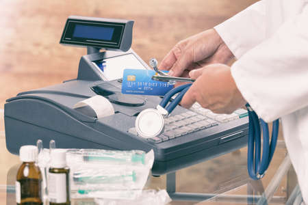 pharmacist or medical doctor holdnig stethoscope and using cash register and credit card at pharmacy...