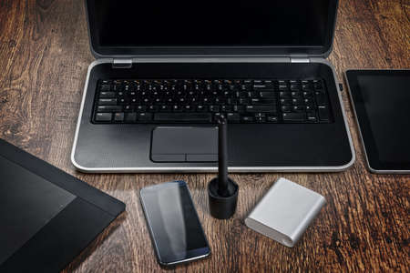 Top view of office desk with laptop computer, mobile phone, graphic tablet with pen and power bank