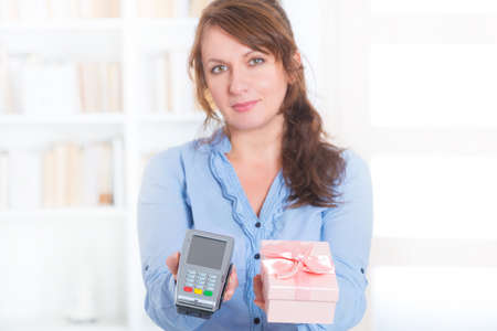 Smiling woman seller gives payment terminal and goods to the client to pay for