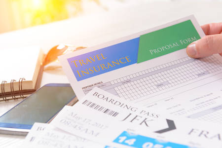 Airline boarding pass tickets in hand with travel insurance, sunglasses, pen and notebook as a concept of travelingの写真素材