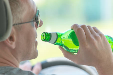 Man driving a car with a bottle of beer or other alcohol drink. Don't drink and drive conceptの写真素材