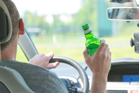 Man driving a car with a bottle of beer or other alcohol drink. Don't drink and drive concept