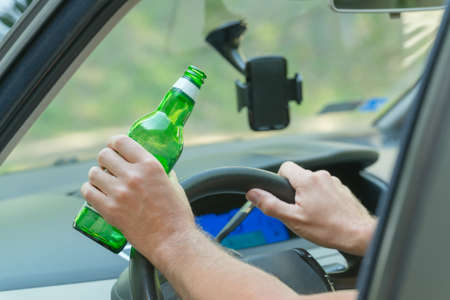 Man holding green bottle of beer in hand while driving a car. Don't drink and drive conceptの写真素材