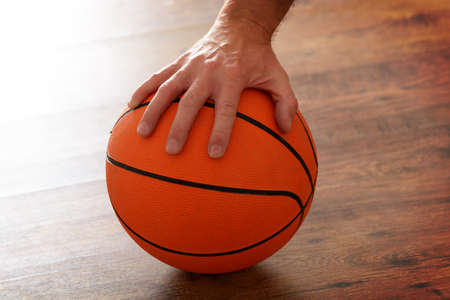 Basketball hold by one male hand on wooden floorの写真素材