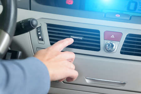 Driver hand tuning air ventilation grille, emergency flasher switch and light in modern car interiorの写真素材