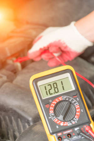 Car mechanic uses a multimeter to check car battery voltage