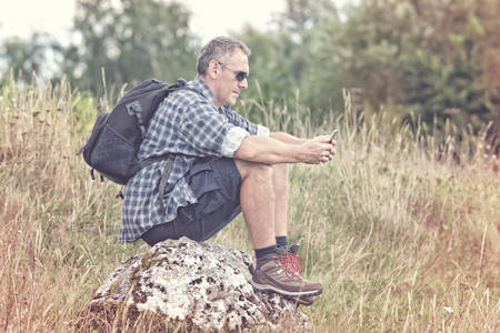 Man backpacker sitting on a rock with smartphoneの写真素材