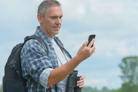 Man backpacker using smart phone and holding binoculars