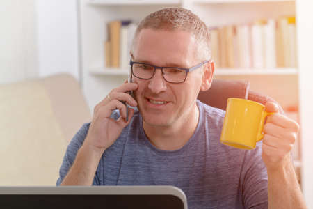 Freelancer working on laptop computer while talking on the smart-phone at home or office