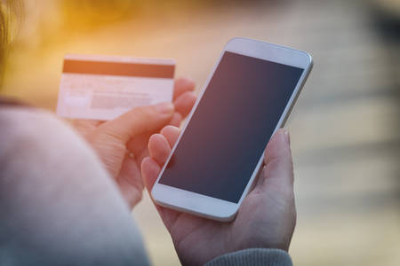 Hands holding credit card and using smart phone outdoor, mobile online payment concept