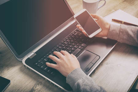 Concept of modern working style. Hand holding smartphone and other one on laptop keyboard