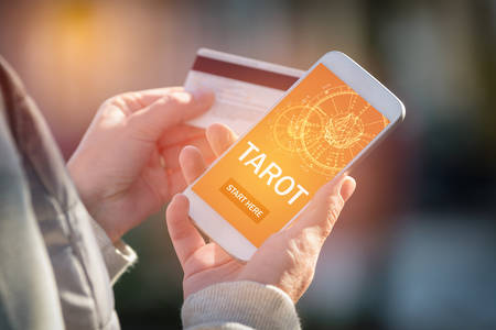 Smartphone with modern fortunetelling application on screen and hand with a credit card ready to pay...