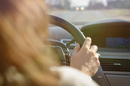 Woman driving a car, close up of her hand at the steering wheel. View from behind