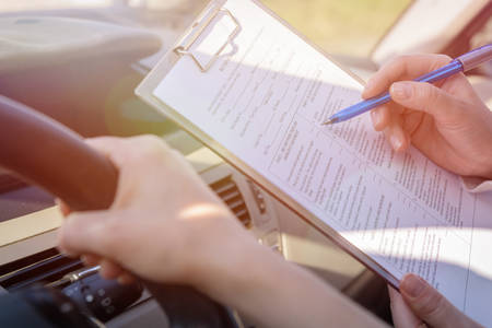 Examiner filling in driver's license road test form sitting with her student inside a car