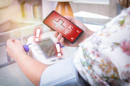 Woman measuring blood pressure at home and using simple user-friendly smart phone application to call rescue team to prevent heart attackの写真素材