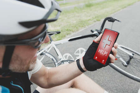 Injured biker holding his smartphone calling rescue team with simple user-friendly smart phone...