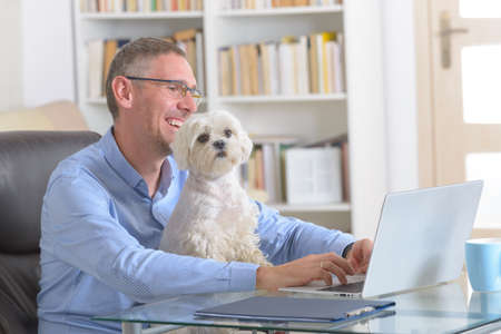 Man working at home or office and holding his liitle dog.