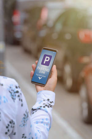 Woman using smartphone app to pay for parking in the paid parking zone in a city