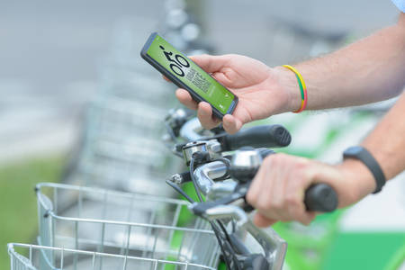 Man is using smart phone to rent bicycle from urban bicycle sharing station