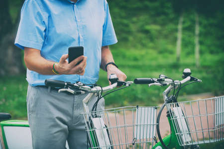 Man is using smart phone to rent bicycle from urban bicycle sharing stationの写真素材