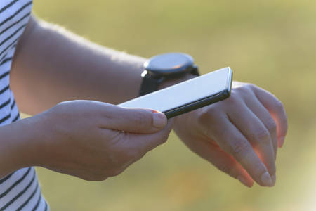 Woman uses the smartwatch and smart phone to check the latest notifications and messages outside