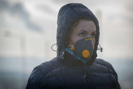 Woman wearing a real anti-pollution, anti-smog and viruses face mask; dense smog in air.の写真素材
