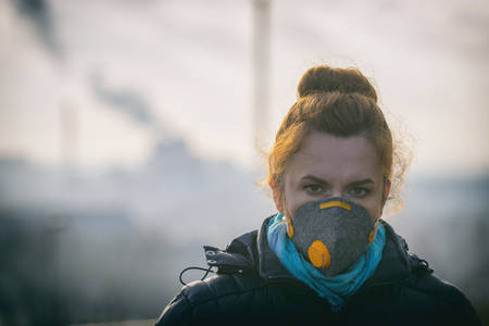 Woman wearing a real anti-pollution, anti-smog and viruses face mask; dense smog in air.の写真素材