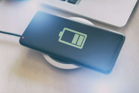 Smartphone in hand near a wireless charging pad, charger.の写真素材