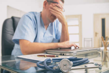 Overworked doctor sitting in his office. Focus on stethoscope in foreground