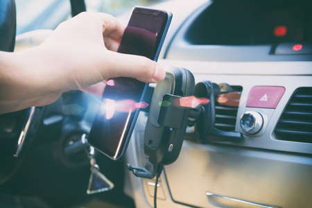 Modern wireless smartphone charging in a car with a hand putting a phone on it. Dashboard in background.の写真素材