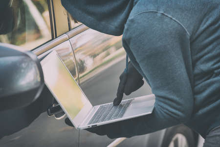 Hooded thief tries to break the car's security systems with laptop. Hacking modern car conceptの写真素材