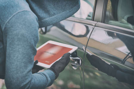 Hooded thief tries to break the car's security systems with tablet. Hacking modern car conceptの写真素材
