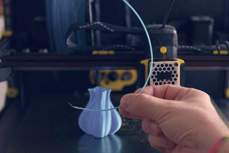 Modern 3d printer with printed three dimentional model of vase. Hand holding filament in the foregroundの写真素材