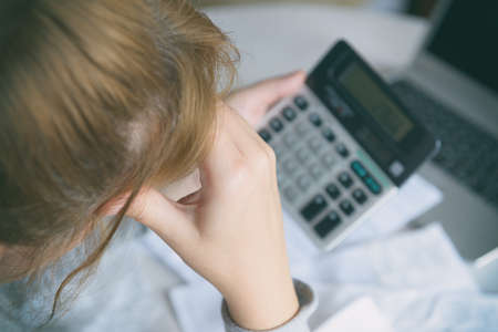 Woman uses a calculator to sum up expenses and holds her head worrying about the amount of money spentの写真素材