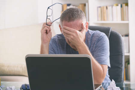 Tired and overworked freelancer holding his head in hand while sitting at his working place in the...
