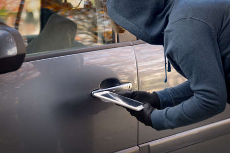 Hooded thief tries to break the car's security systems with tablet. Hacking modern car concept