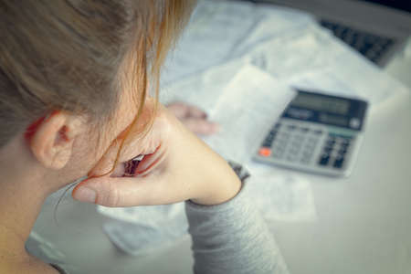 Woman uses a calculator to sum up expenses and holds her head worrying about the amount of money spentの写真素材