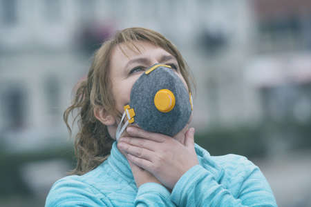 Woman wearing a real anti-pollution, anti-smog and viruses face mask; dense smog in air.