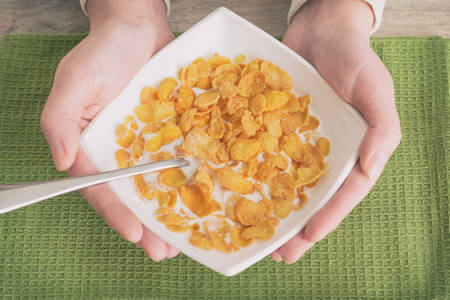 Female hands holding bowl with healthy breakfast made of cornflakes with milkの写真素材